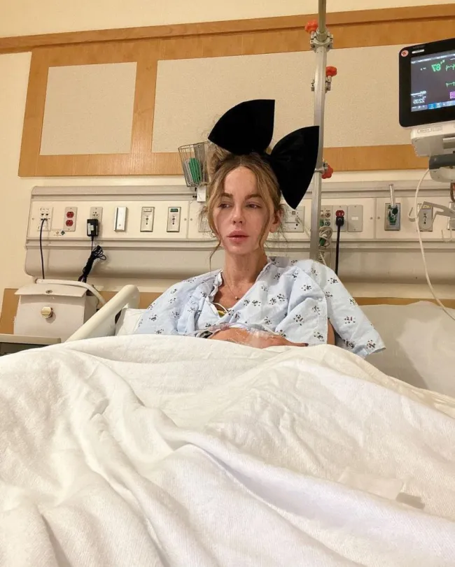 Kate Beckinsale con un enorme lazo en el pelo en la cama de un hospital.