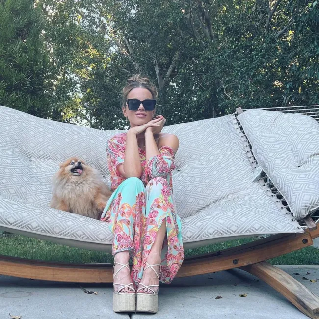 Kate Beckinsale sentada con un vestido largo en una hamaca con un perro.