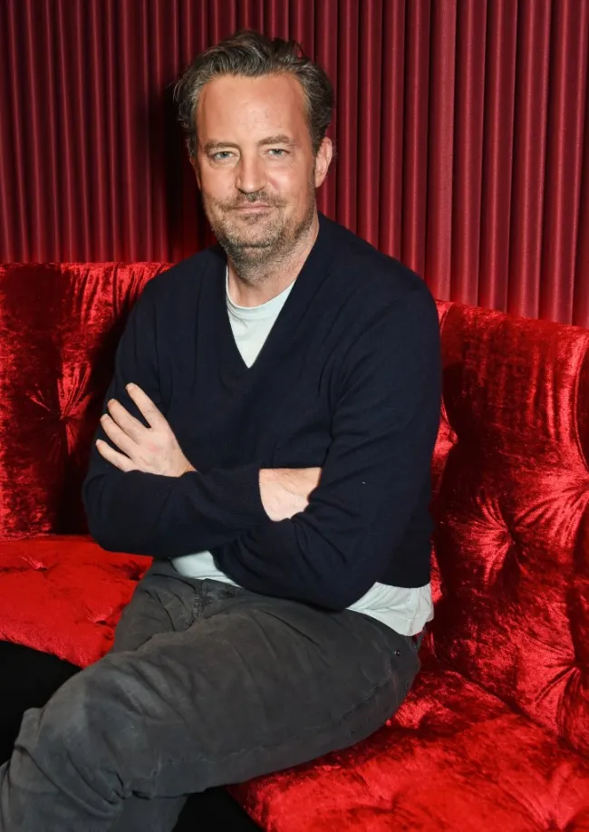 matthew perry sentado en una silla de banquete roja