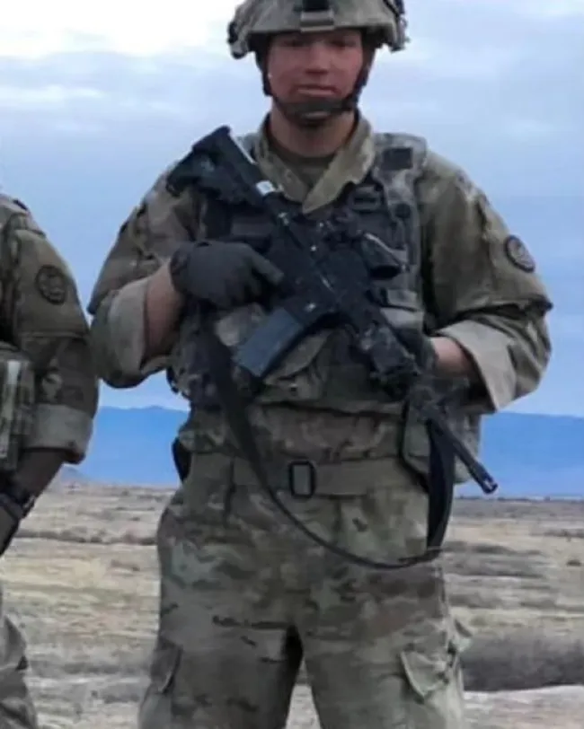 Garrison Brown con uniforme militar y sosteniendo un rifle.
