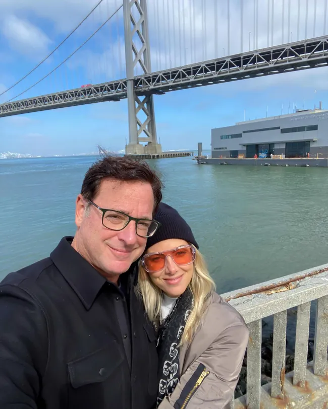 Bob Saget y Kelly Rizzo selfie frente a un puente