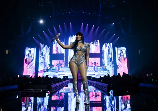 Nicki Minaj sonriendo en el escenario con un precioso mono plateado cromado y botas plateadas a juego.