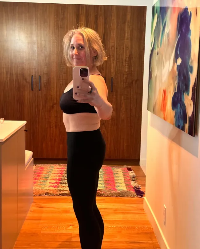 Selfie en el espejo de Ricki Lake con un sujetador deportivo negro y leggings