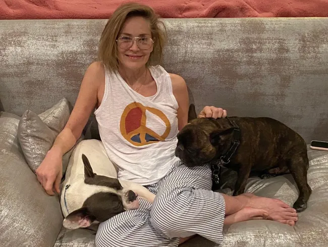 Sharon Stone sin maquillaje sentada en el sofá con sus perros