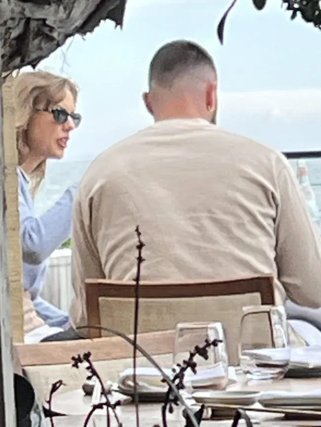 Taylor Swift conversando con Travis Kelce en una mesa de restaurante.