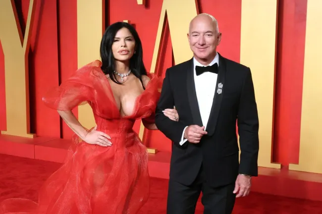 Lauren Sánchez, con vestido rojo, se toma del brazo con Jeff Bezos, con esmoquin.