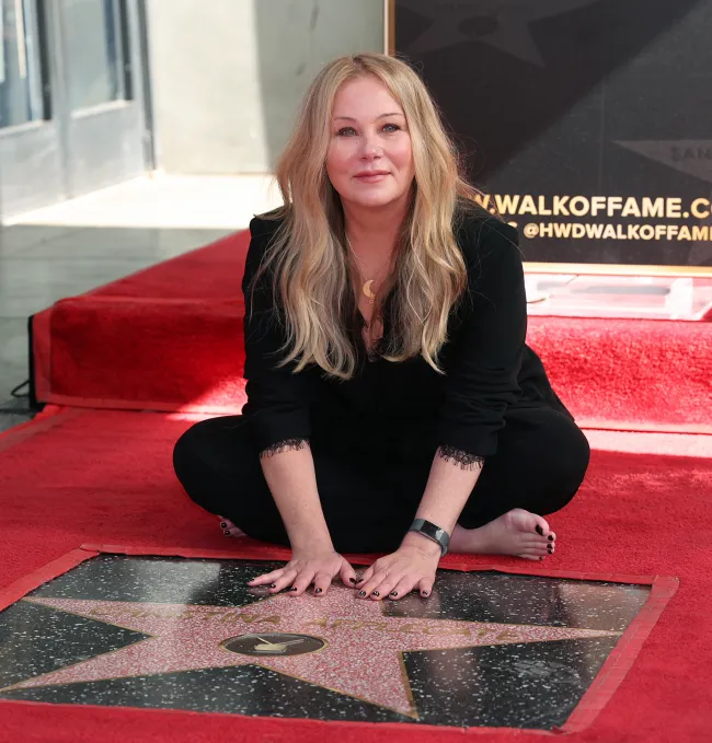 Christina Applegate en cuclillas frente a su estrella del Paseo de la Fama de Hollywood