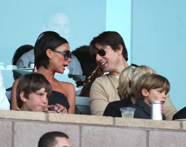 Victoria Beckham habla con Tom Cruise, mientras Romeo Beckham se sienta en el regazo de su abuela Sandra Beckham.