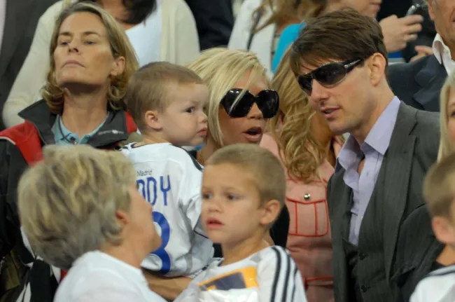 Tom Cruise habla con Victoria Beckham, sosteniendo a Cruz Beckham. Sandra Beckham sostiene a Romeo Beckham.