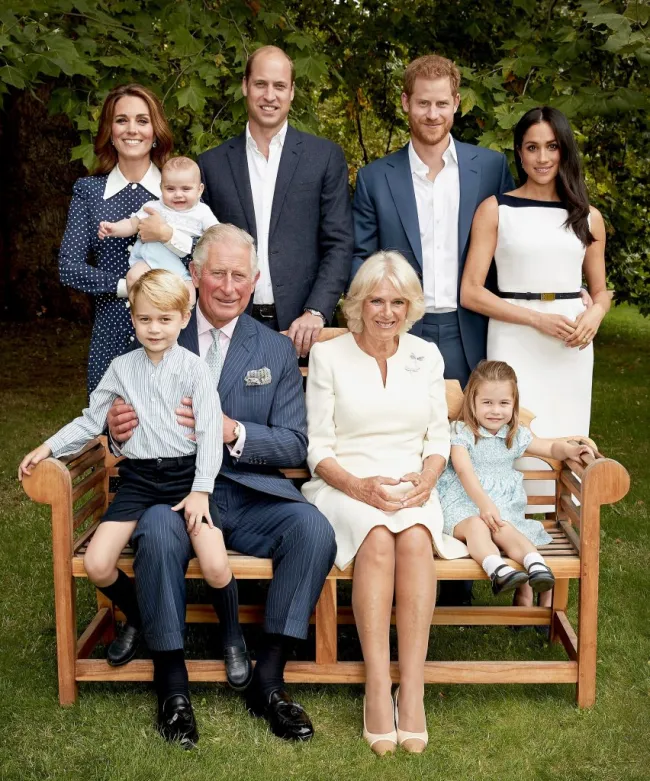 El rey Carlos sostiene al príncipe George, la reina Camilla se sienta junto a la princesa Charlotte. Kate Middleton sostiene al bebé Príncipe Archie y está junto al Príncipe William, quien está junto al Príncipe Harry y Meghan Markle.
