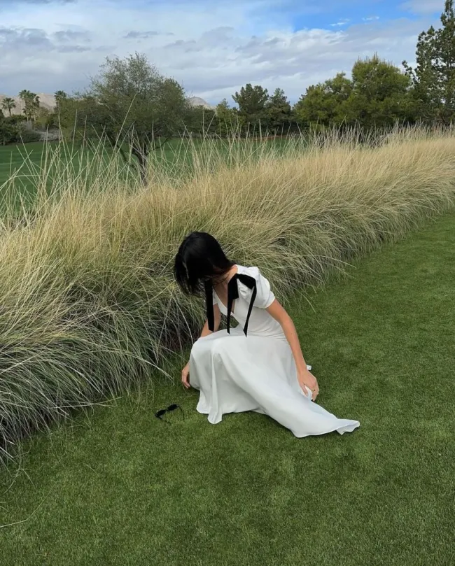 Kendall Jenner se inclina para recoger gafas de sol en el campo con un vestido de seda blanco.