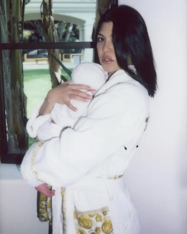 Kourtney Kardashian en bata sosteniendo a su bebé