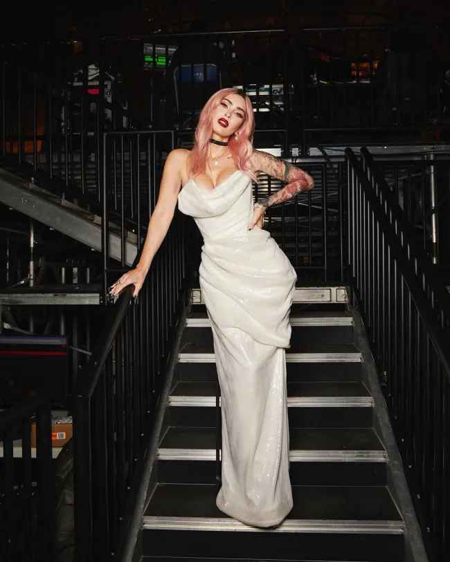 Megan Fox posando con un vestido blanco en unas escaleras.