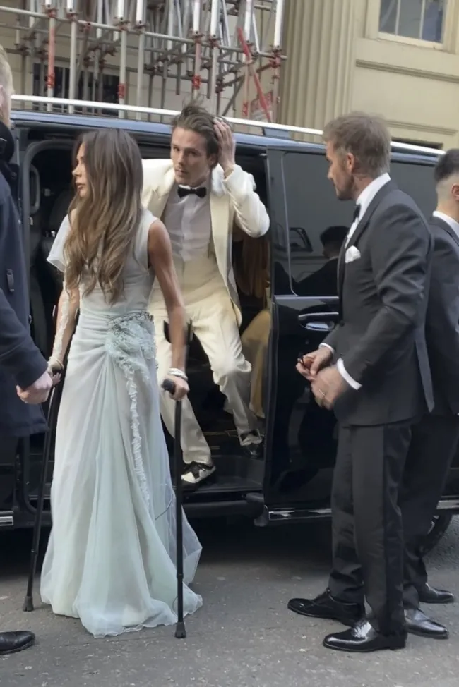 Victoria Beckham con muletas, Brooklyn Beckham bajándose del coche y David Beckham parado junto al coche.
