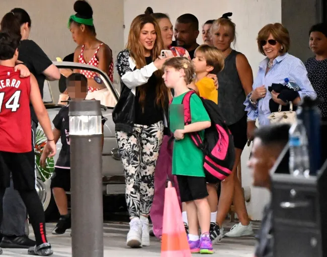 Shakira vista vestida de manera informal y con sus dos hijos rodeada de otros padres y niños afuera de una escuela