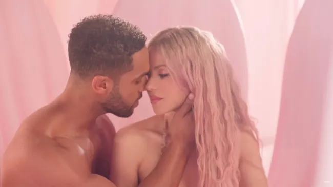 Shakira con cabello rosado y hombros desnudos aparentemente besando a un hombre en topless