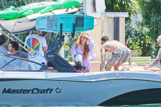 Shakira con un vestido color lavanda en la parte trasera de un gran barco, recibida por un hombre vestido sólo con pantalones cortos y con tatuajes en todo el cuerpo visibles.