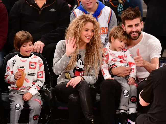 Shakira, vestida con un jersey de Mickey Mouse y pantalones de cuero negros, saluda mientras su ex Gerard Piqué levanta el pulgar mientras sostiene a su hijo menor en su regazo. Su hijo mayor está sentado a su izquierda.