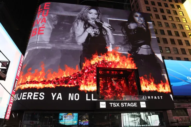 Una pantalla gigante en un edificio de Times Square muestra a Shakira cantando con llamas al frente.