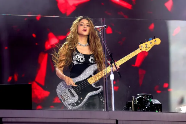 Shakira vestida de negro tocando una guitarra en un escenario al aire libre