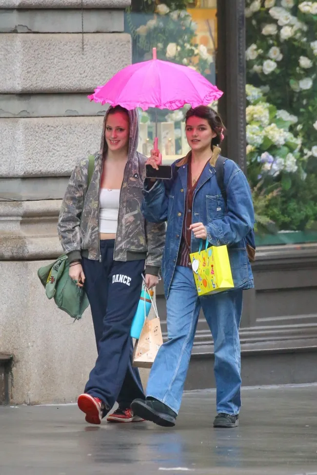 Suri Cruise caminando con un amigo bajo la lluvia mientras sostiene un paraguas.