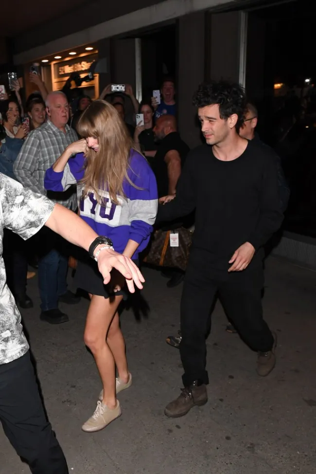 Taylor Swift y Matty Healy caminando entre la multitud por la noche