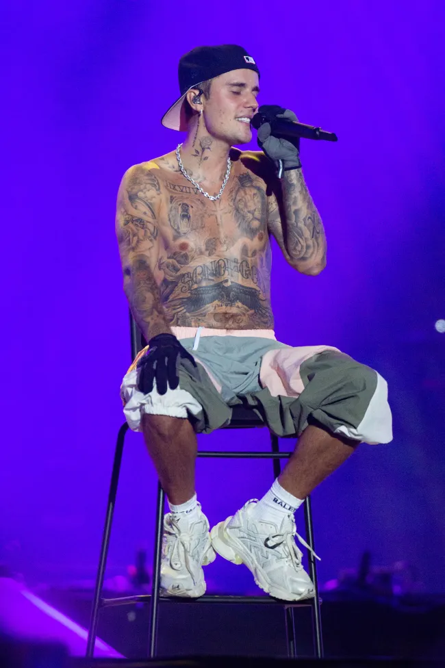 Justin Bieber sin camisa cantando en un taburete.