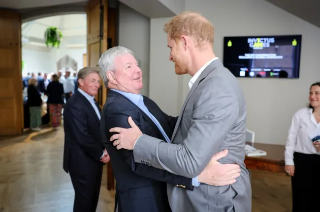 El príncipe Harry saluda a Sir Keith Mills con un abrazo.