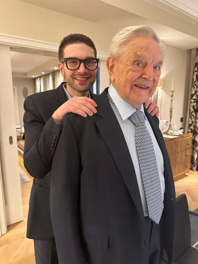 Alex Soros apoya sus manos sobre los hombros de su padre George Soros.
